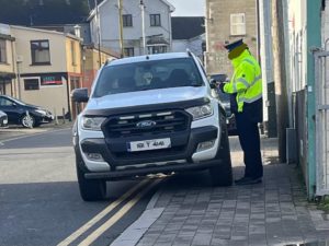 A hero traffic warden in a high visibility jacket giving a ticket to one of those awful US-style Ford pickups who is parked on a footpath. 